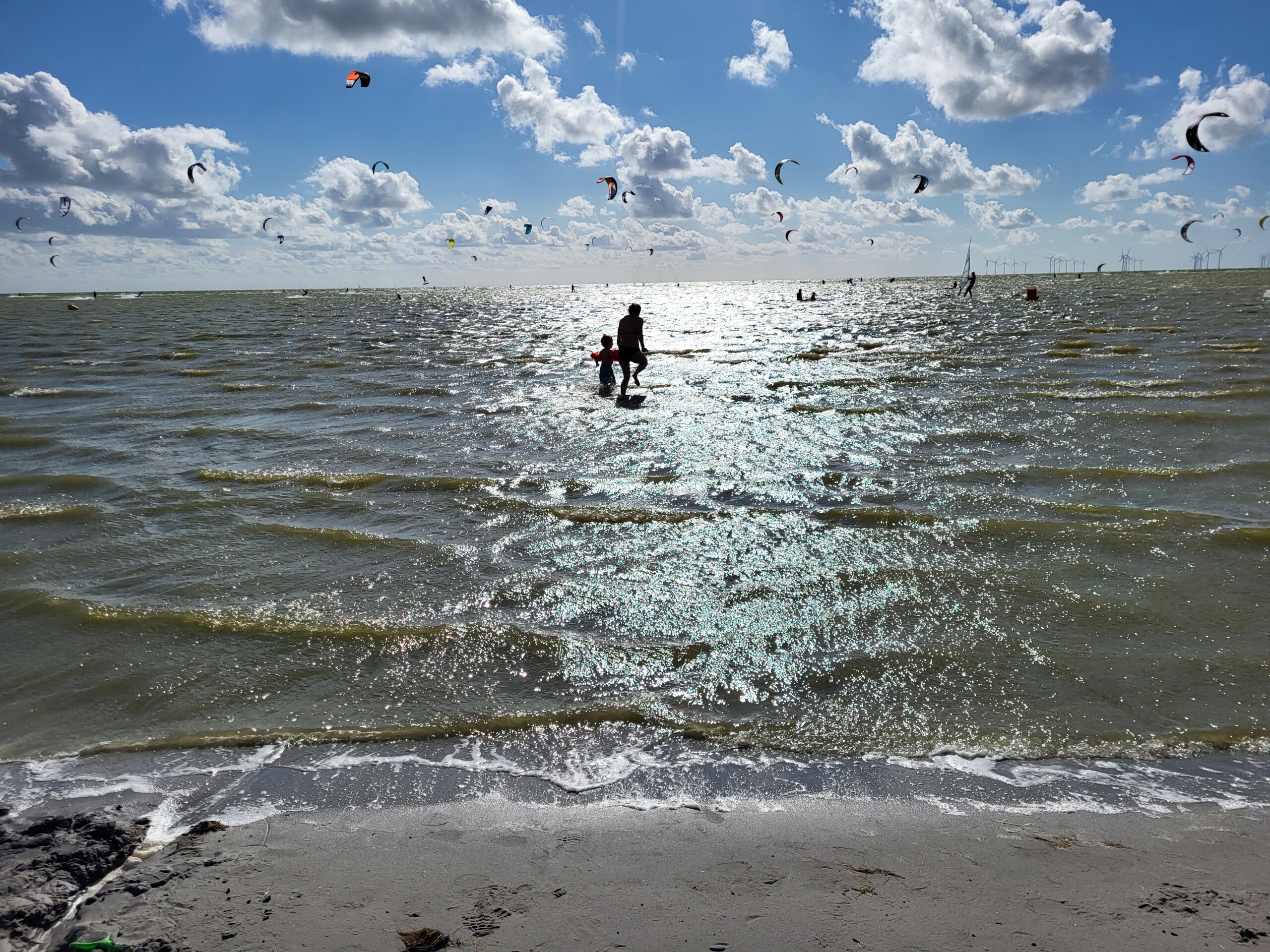 Meer mit vielen Paraglidern und ein Papa mit seinem Sohn im Wasser - dein nächstes Reiseziel mit Ruwwe Camping